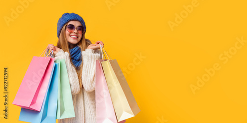 Season of sales. Happy young woman in knitted hat and sunglasses with shopping bags, pink studio background, panorama with empty space