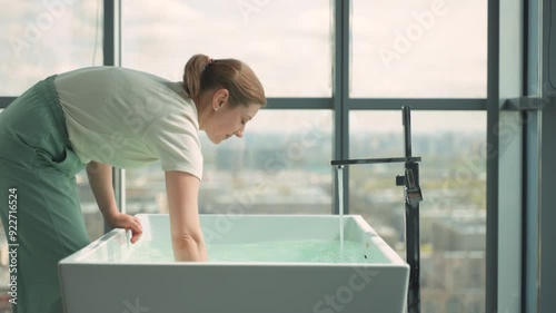 Woman prepares bath for baby, ensuring proper temperature with orange thermometer. Activity fosters child early experiences with water. Concept of infant early development and childhood growth