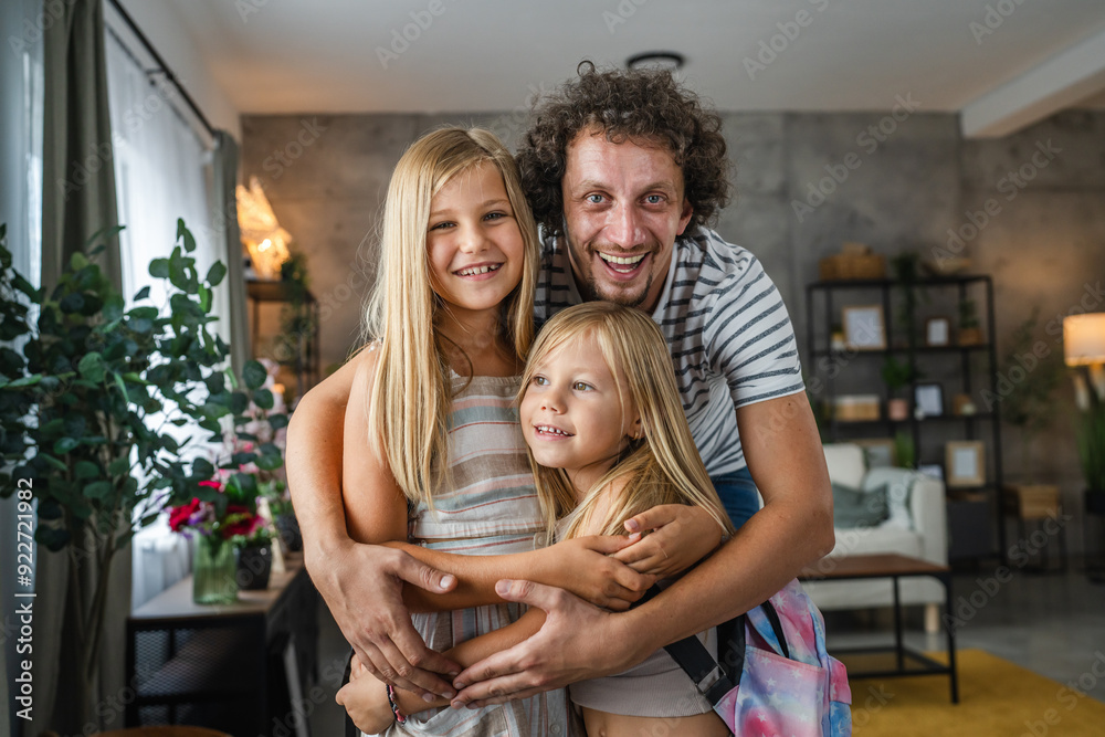 Portrait of daughters and dad stand and hug with backpacks at home