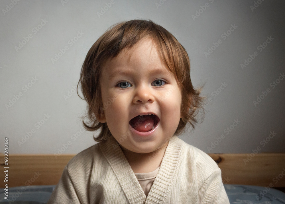 Adorable bebé sonriendo sentado en la cama en el dormitorio con la boca abierta. Interior de la casa Adorable bebé sonriendo sentado en la cama en el dormitorio con la boca abierta. Interior de la casa