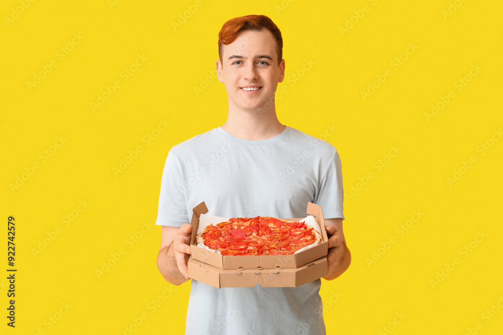 Young man holding cardboard box with tasty pizza on yellow background