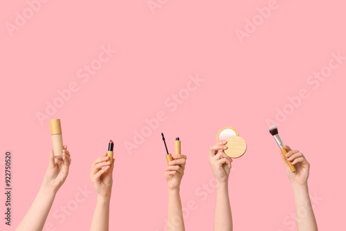 Female hands with makeup foundation, lipstick, mascara, highlighter and brush on pink background