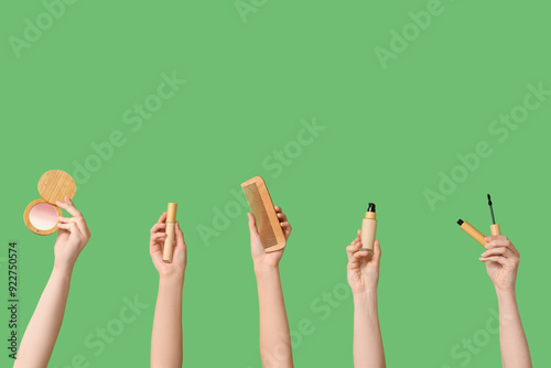 Female hands with highlighter, wooden comb, concealer, foundation and mascara on green background