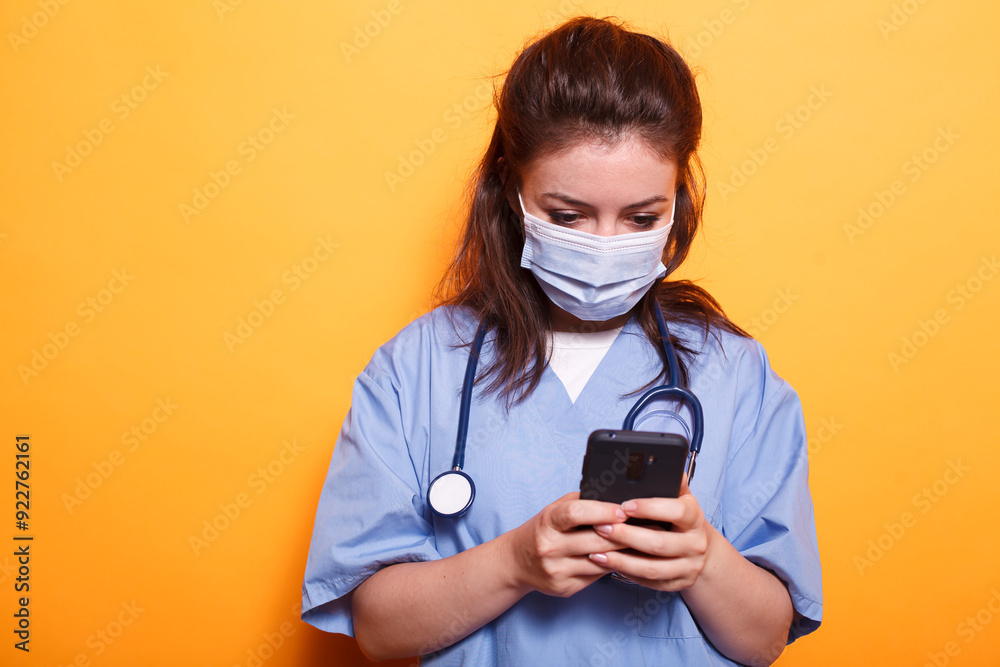 Caucasian female doctor utilizing modern technology while wearing face mask against coronavirus. Medical assistant with stethoscope texting on her mobile phone during pandemic. Caucasian female doctor utilizing modern technology while wearing face mask against coronavirus. Medical assistant with stethoscope texting on her mobile phone during pandemic.