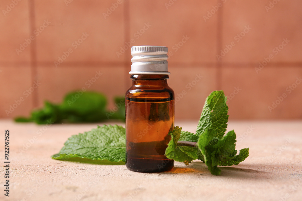 Bottle of essential mint oil and green leaves on pink grunge background, closeup Bottle of essential mint oil and green leaves on pink grunge background, closeup