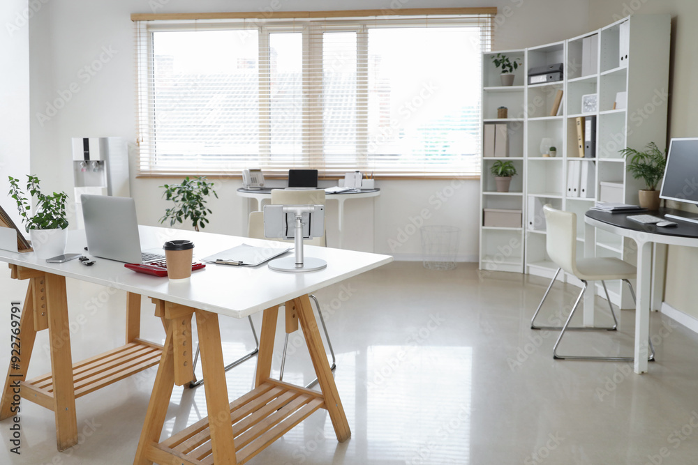 Interior of stylish office with workplaces, laptop and shelving unit Interior of stylish office with workplaces, laptop and shelving unit