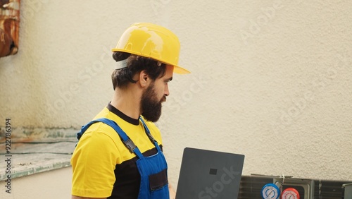 Expert repairman using laptop to look online for new capacitor after finding outdoor air conditioner malfunctioning internal component during customer comissioned maintenance photo