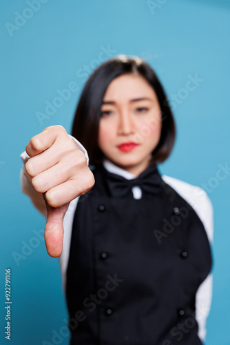 Dissatisfied asian waitress showing thumb down sign, expressing negative feedback and disapproval portrait. Receptionist displaying bad service experience concept and looking at camera