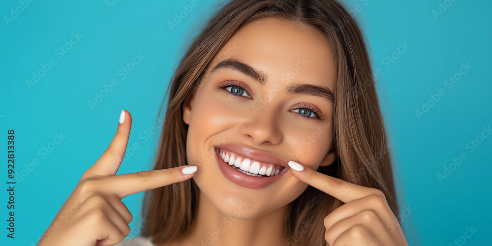 Young woman pointing at her perfect smile on blue background Young woman pointing at her perfect smile on blue background