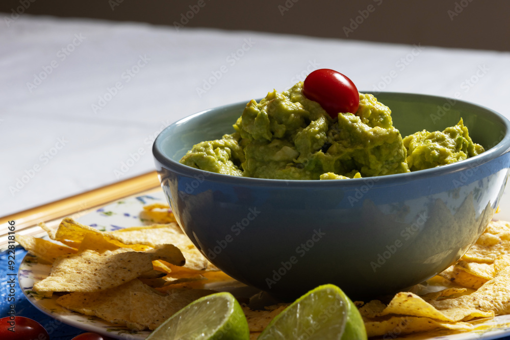 Guacamole in a blue bowl with a cherry tomato on top surrounded by nachos Guacamole in a blue bowl with a cherry tomato on top surrounded by nachos