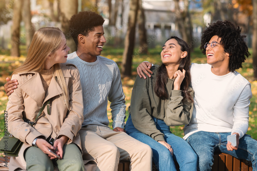 Two mixed race teen couples sitting on bench in public park, having fun Two mixed race teen couples sitting on bench in public park, having fun