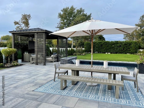 High-end outdoor living space, a backyard patio with pergola, outdoor rug,  tequila bar, dining set, couch, television, pool with waterfall, umbrella, fire pit and stunning grey patio. Modern vibe.