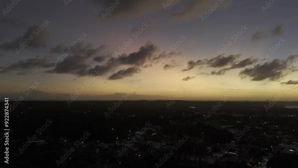 Drone flies backwards at an angle over city lights under orange, pink, and blue sky after sunset in Pipa, Rio Grande do Norte, Brazil Drone flies backwards at an angle over city lights under orange, pink, and blue sky after sunset in Pipa, Rio Grande do Norte, Brazil