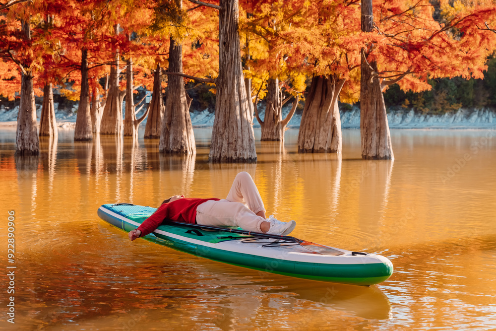 Φωτογραφία Traveller woman lies on stand up paddle board at the lake between trees in autum