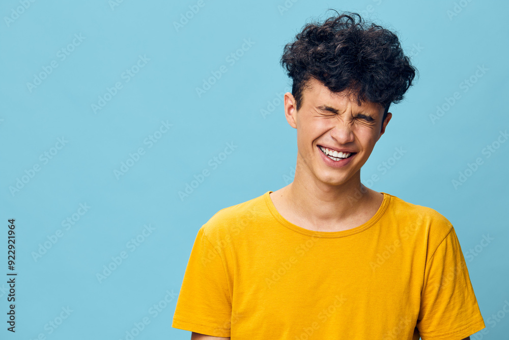 Happy young man smiling with closed eyes wearing a yellow t shirt against a light blue background, conveying joy and positivity in a cheerful concept Happy young man smiling with closed eyes wearing a yellow t shirt against a light blue background, conveying joy and positivity in a cheerful concept