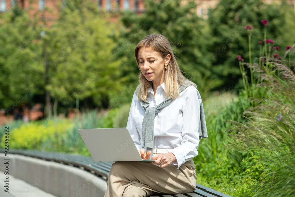 Focused businesswoman with laptop dealing with work issues outside in open fresh air in public park. Female freelancer spends time outdoors working on project at computer. Lady typing, communicating. Focused businesswoman with laptop dealing with work issues outside in open fresh air in public park. Female freelancer spends time outdoors working on project at computer. Lady typing, communicating.