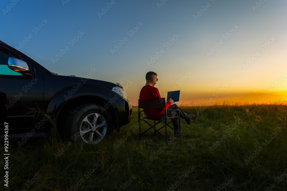 Naklejka premium Man using laptop while sitting at nature. Freelance work, remote work during vacation