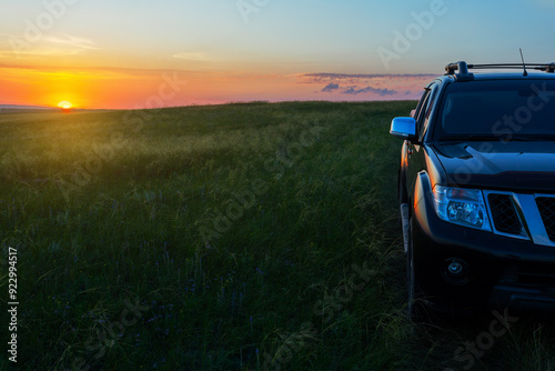 SUV driving on meadow hill off-roads at sunset. Summer auto travel concept background with copy space