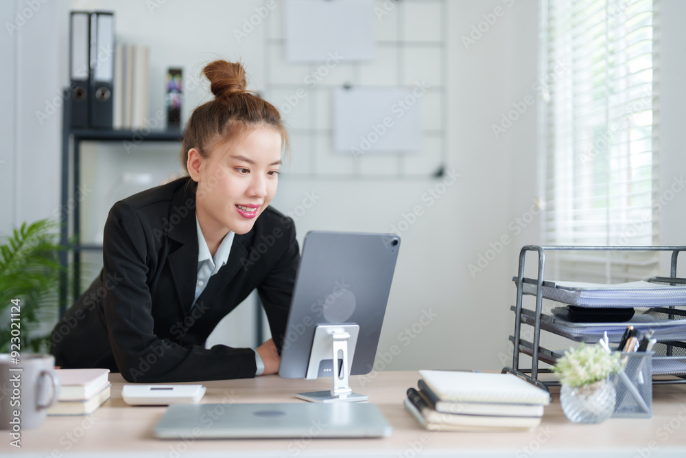 A businesswoman in a black suit is leaning over her desk, deeply focused on her work in a modern office environment A businesswoman in a black suit is leaning over her desk, deeply focused on her work in a modern office environment