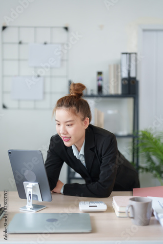 A businesswoman in a black suit is leaning over her desk, deeply focused on her work in a modern office environment