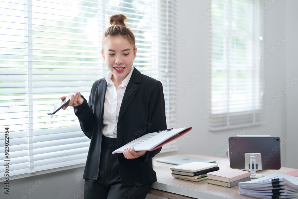 A businesswoman in a black suit is standing by the window, holding a clipboard and a pen, looking prepared and ready to take notes in the office A businesswoman in a black suit is standing by the window, holding a clipboard and a pen, looking prepared and ready to take notes in the office