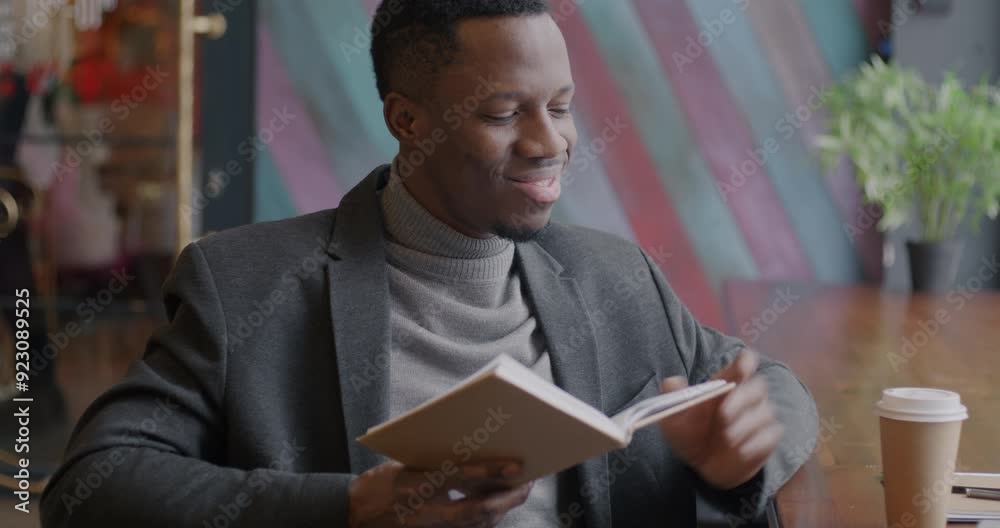 Cheerful African American entrepreneur reading book relaxing and drinking coffee in modern cafe. Intelligent hobby and lifestyle concept. Cheerful African American entrepreneur reading book relaxing and drinking coffee in modern cafe. Intelligent hobby and lifestyle concept.