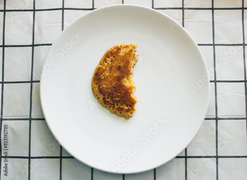 Selective focus half eaten pancakes on a white plate on a black and white checkered dining table