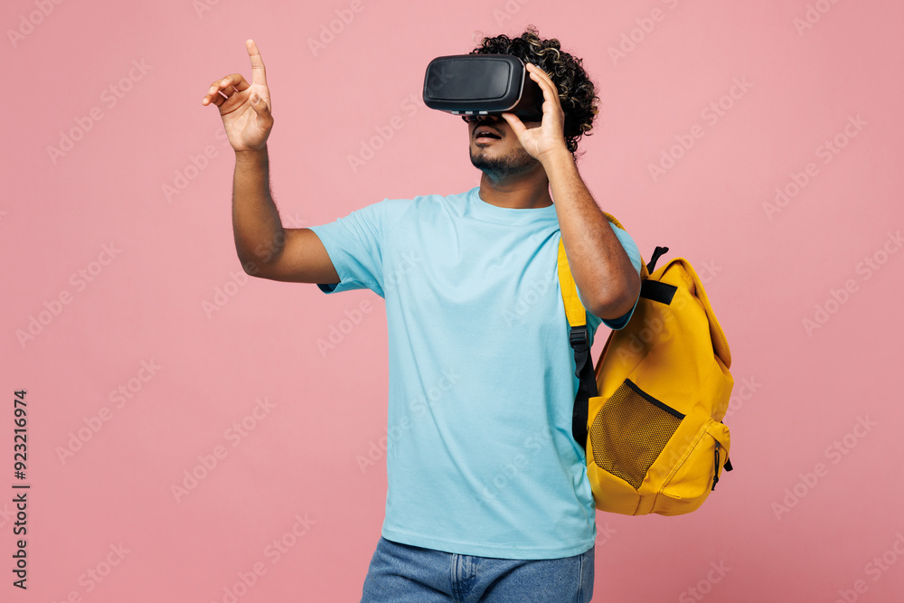 Young smart Indian boy student he wear blue t-shirt casual clothes backpack bag watching in vr headset pc gadget spread hand isolated on plain pink background. High school university college concept.
