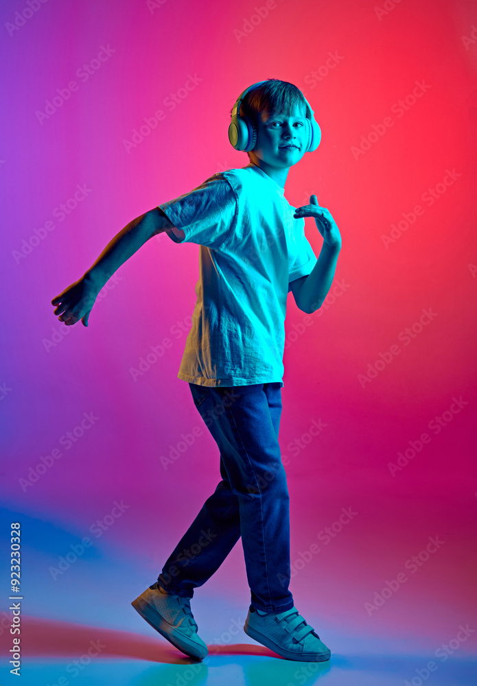 Young little boy dressed casual outfit dancing in headphones in neon light against gradient blue-pink studio background. Concept of children, human emotions, fashion and style, lifestyle. Ad Young little boy dressed casual outfit dancing in headphones in neon light against gradient blue-pink studio background. Concept of children, human emotions, fashion and style, lifestyle. Ad