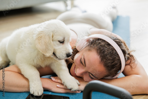 Young woman playing is interrupted to play by her golden retriever dog puppy while doing sports at home. Young woman listens to music with her headphones.