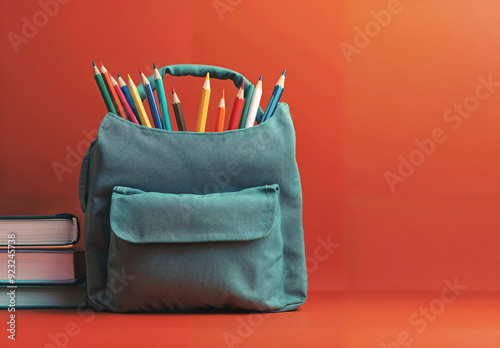 Green backpack, colorful pencils, stack of books on red background with copy space