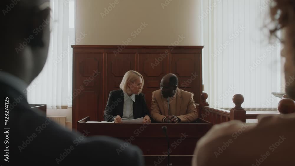 Over the shoulder view of Black male complainant and Caucasian female prosecutor discussing points of case at court session Over the shoulder view of Black male complainant and Caucasian female prosecutor discussing points of case at court session