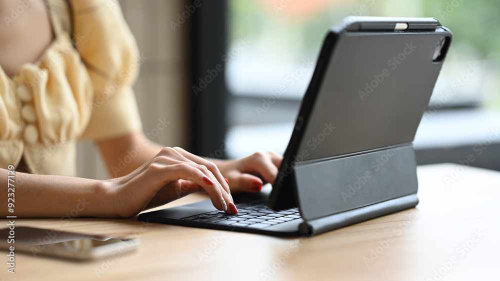 Fototapeta premium Cropped shot of woman typing on black keyboard of digital tablet, working remotely at cafe
