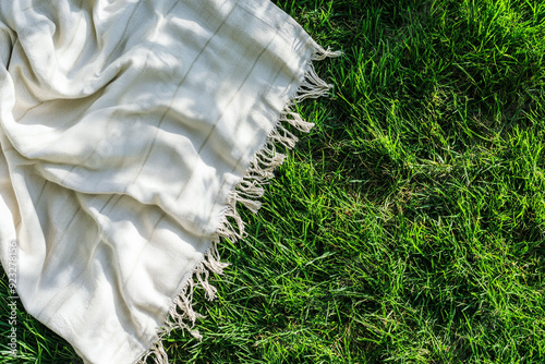 Fototapeta Naklejka Na Ścianę i Meble -  White picnic blanket on a green grass from top view