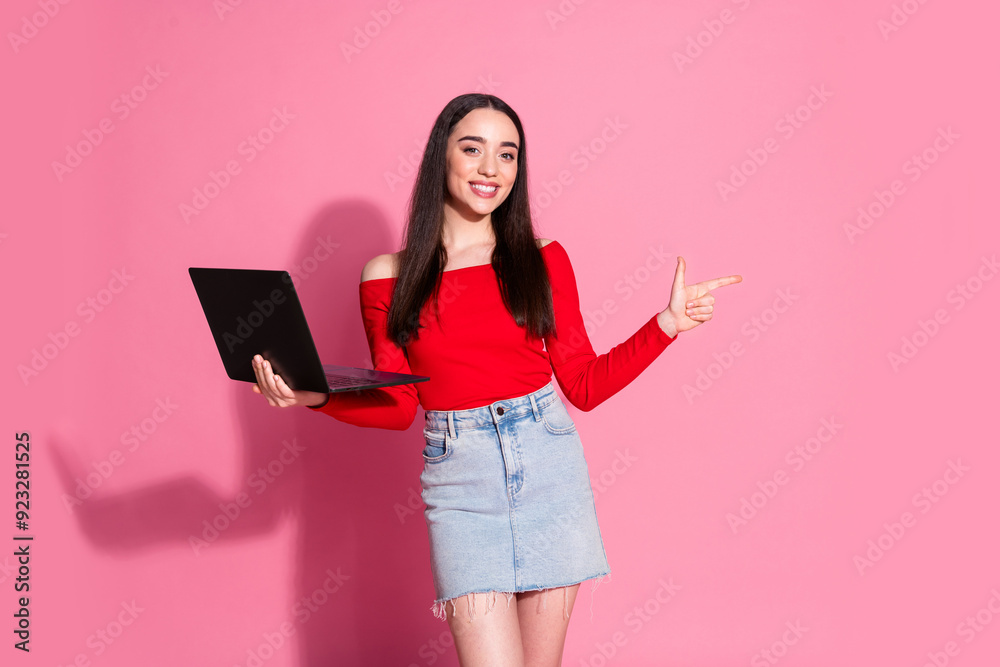 Photo of gorgeous young woman laptop direct finger empty space red shirt isolated on pink color background Photo of gorgeous young woman laptop direct finger empty space red shirt isolated on pink color background