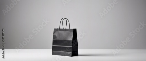 Black shopping bag standing on a white surface, minimalist style, grey background, concept of shopping and retail photo