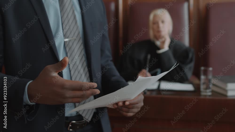 Close up shot of hands of unrecognisable male lawyer holding juridical document defending suspect during court session, female judge listening in background