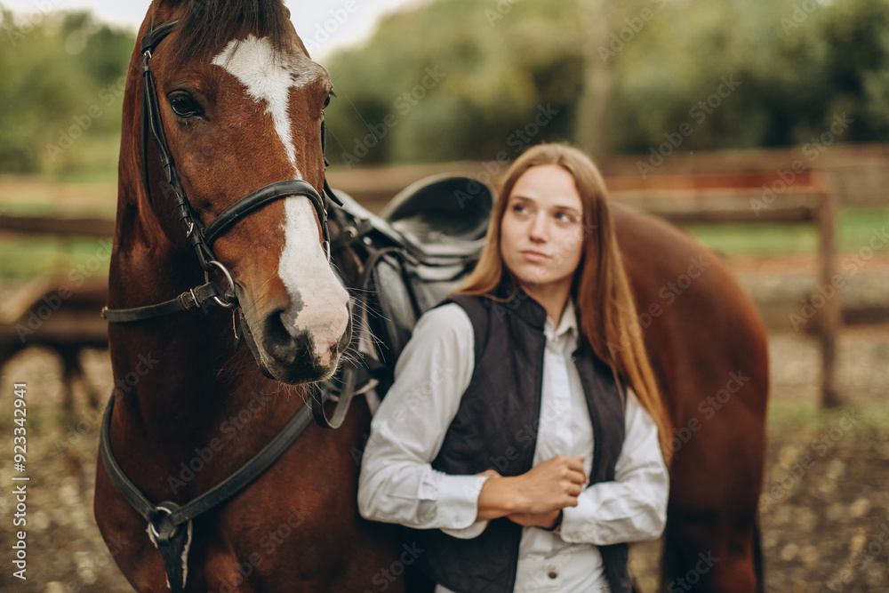 A young female equestrian stands near her horse and prepares for a competition.