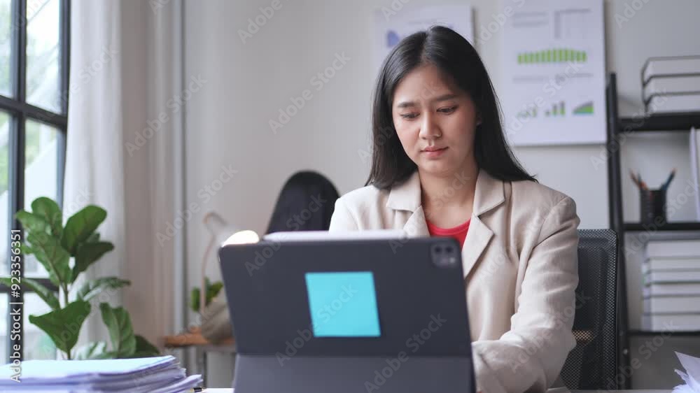 Professional focusing on tasks using a tablet in a contemporary office, seen through various angles. Showing productivity amid a work environment filled with charts, files, and greenery Professional focusing on tasks using a tablet in a contemporary office, seen through various angles. Showing productivity amid a work environment filled with charts, files, and greenery