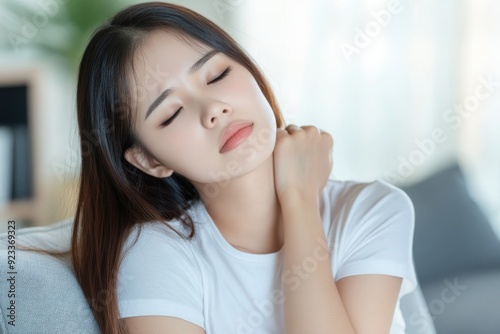 Asian young woman with stiff muscles, back pain, neck ache, rubbing shoulder tenderness, sitting on couch at home with soreness from sitting.Health care and medicine.