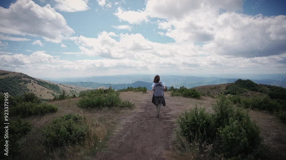 A young female traveler walking away from the camera while walking through beautiful mountains on a windy day A young female traveler walking away from the camera while walking through beautiful mountains on a windy day
