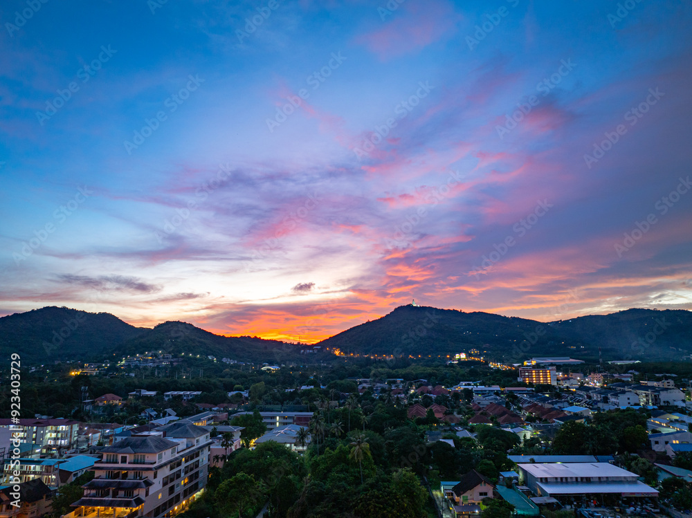 Obraz premium An enchanting aerial view of Phuket city at twilight, with vibrant city lights illuminating the streets. The soft hues of the sky blend seamlessly with the distant horizon, creating a serene
