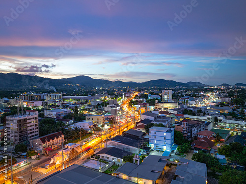 Fototapeta Naklejka Na Ścianę i Meble -  An enchanting aerial view of Phuket city at twilight, with vibrant city lights illuminating the streets. The soft hues of the sky blend seamlessly with the distant horizon, creating a serene