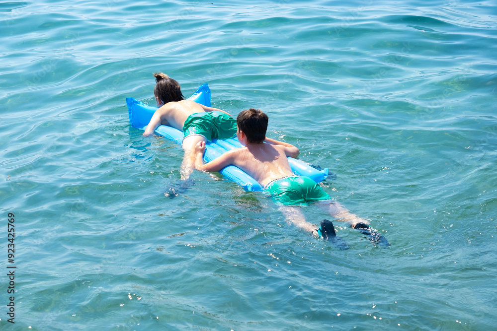 Two children swimming in sea, adrift on blue inflatable raft, accident in open water, inflatable raft swept farther and farther out to sea by strong current, water safety Two children swimming in sea, adrift on blue inflatable raft, accident in open water, inflatable raft swept farther and farther out to sea by strong current, water safety