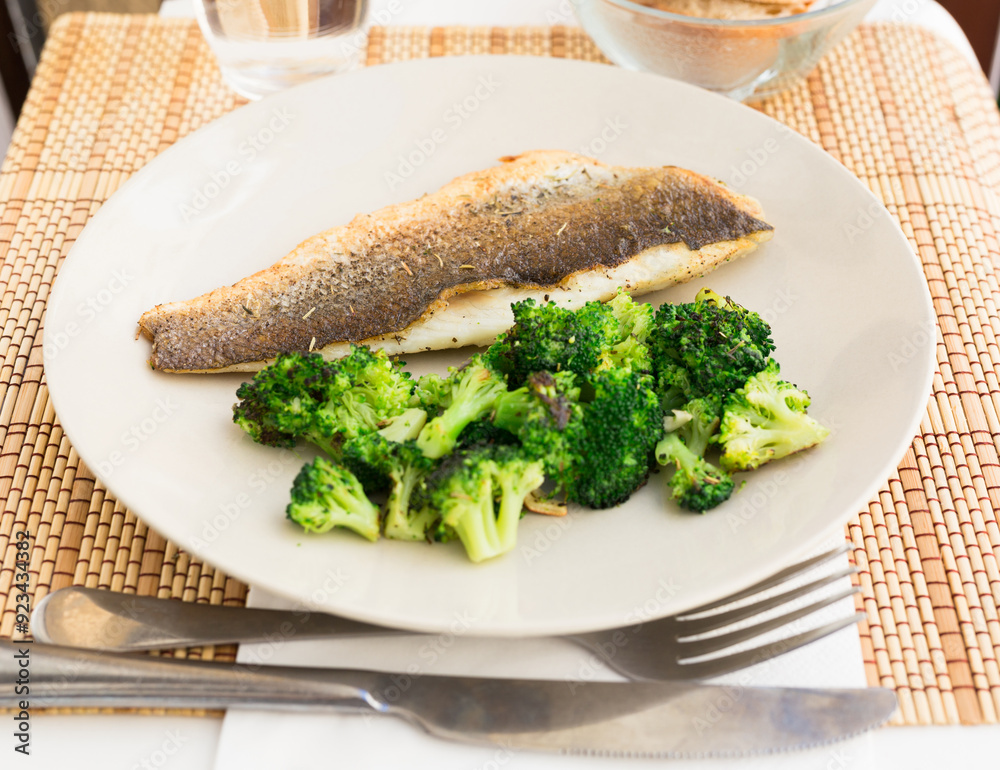 Fried fillet of sea bass with garnish of broccoli on black warm stone plate Fried fillet of sea bass with garnish of broccoli on black warm stone plate