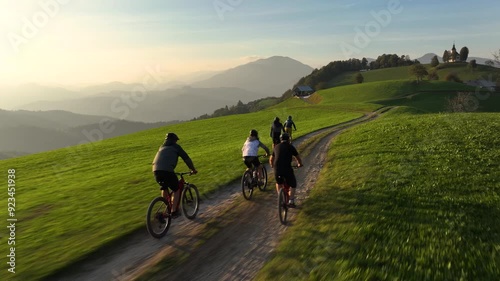 AERIAL: Mountain bikers ride along the hilltop trail on a sunny autumn evening. Scenic drone shot of a group of active tourists riding electric bikes at sunrise. Bike ride in the Slovenian mountains.