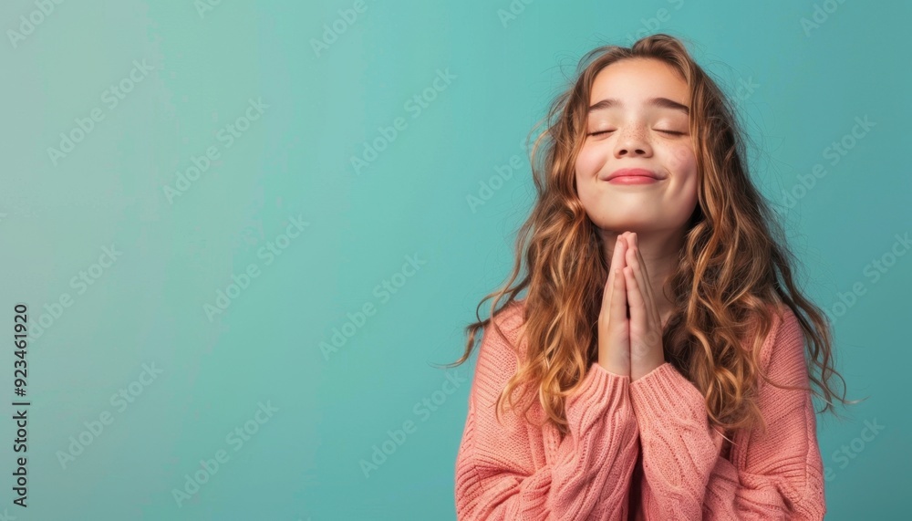 Young girl smiling and expressing gratitude against a soft teal background indoors Young girl smiling and expressing gratitude against a soft teal background indoors