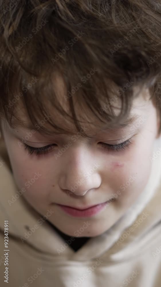 Dark-haired teenage boy looking down and then straight into camera. Close up. Portrait of a kid smiling. Light backdrop. Dark-haired teenage boy looking down and then straight into camera. Close up. Portrait of a kid smiling. Light backdrop.