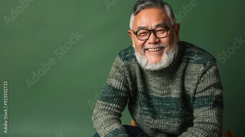 An elderly man with a beard and glasses smiles warmly while sitting comfortably