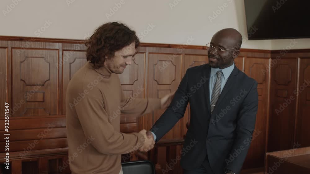 Young defendant and male attorney expressing joy and shaking hands while celebrating victory in court